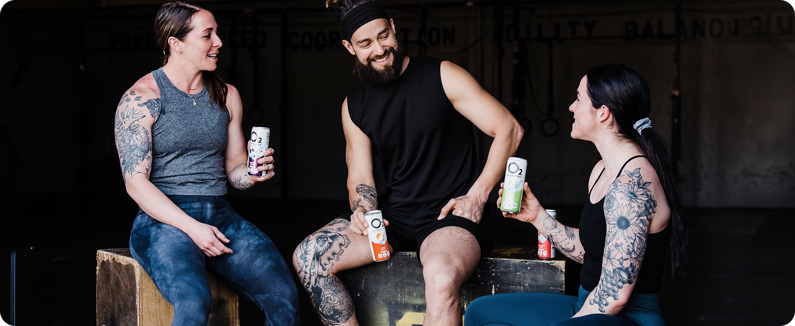 Three people sitting together, each holding a can of O2, with a dark background